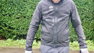 Torso of man wearing black cycling jacket in front of hedge