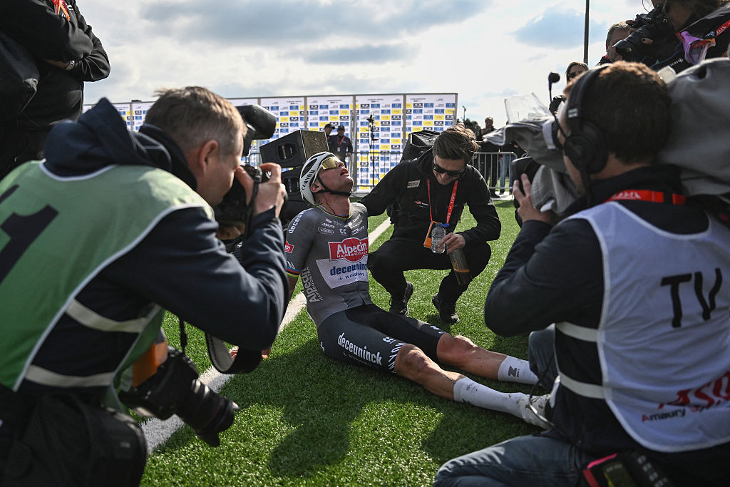 Cámaras y entrenadores rodean a Mathieu van der Poel sentado en el suelo, cansado, al final de la París-Roubaix 2025