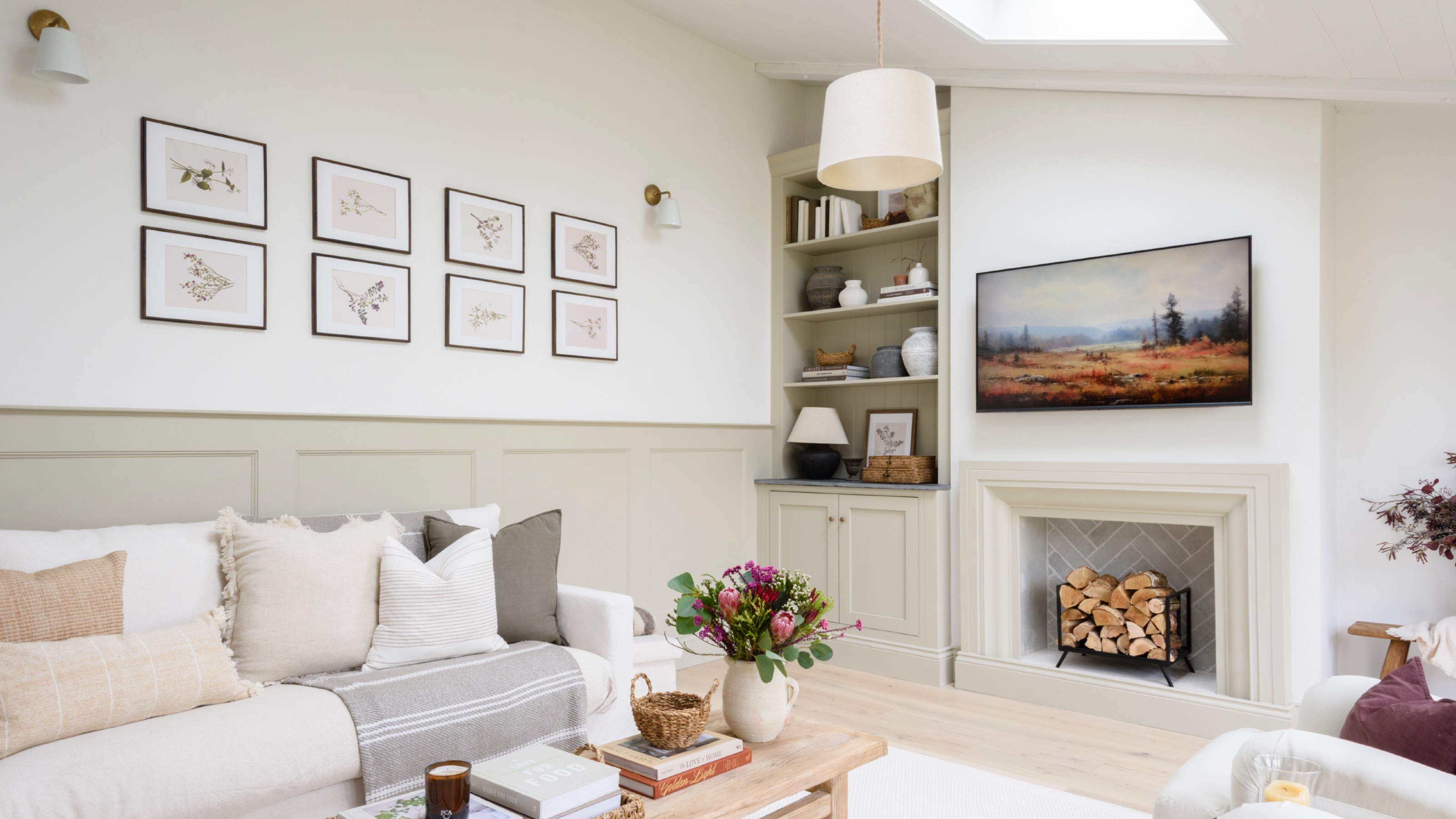 A white living room with half-panelled walls, a white sofa and a layered lighting scheme with wall lights, a table lamp and a ceiling light