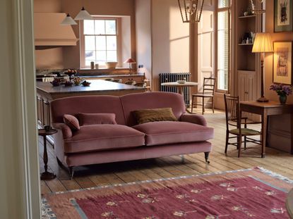 a pink sofa in a light pink living room and kitchen with a pink rug 