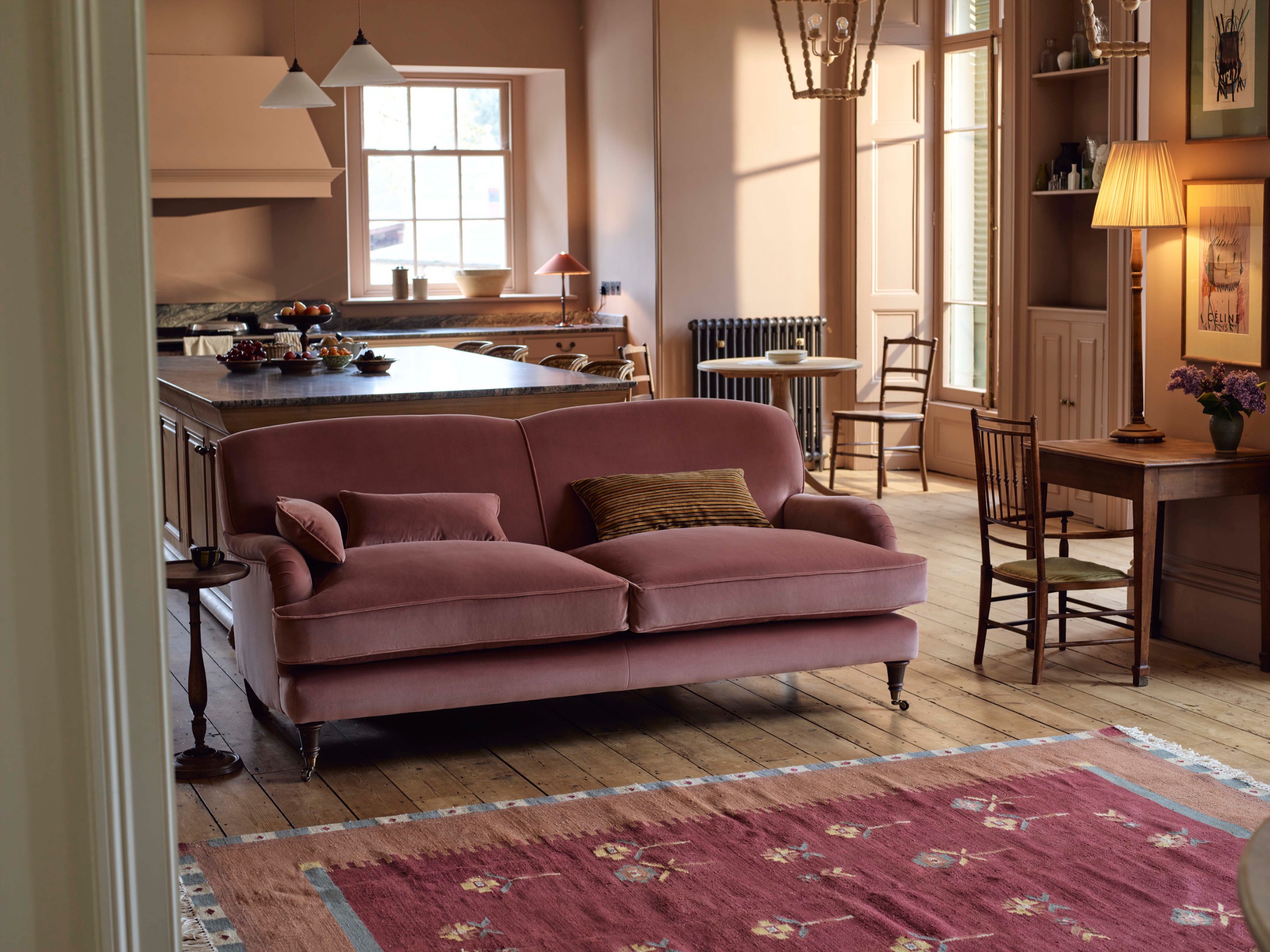 a pink sofa in a light pink living room and kitchen with a pink rug 