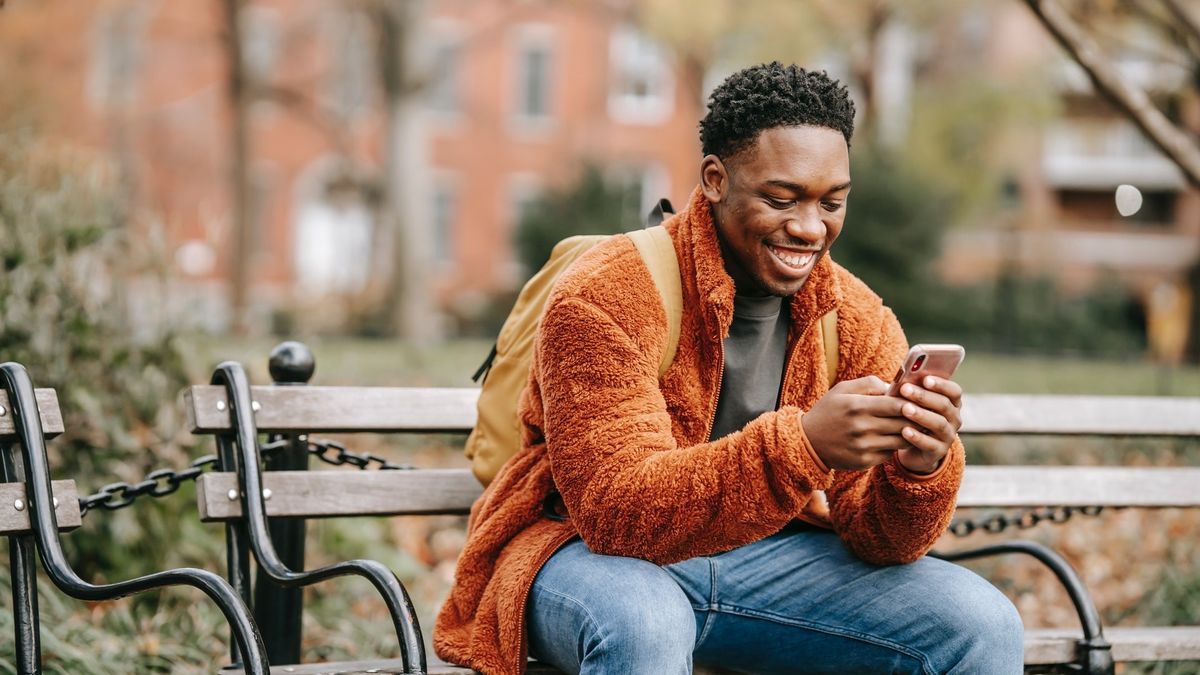 best Huawei phone: Smiling man using his phone on a park bench