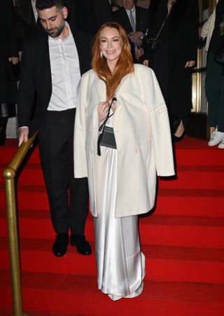 Lindsay Lohan wearing a cream colored wool coat with a white satin gown and a black bag