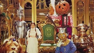 Dorothy, Jack, and scarecrow stand in front of a throne that says Oz