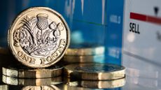 Close up of a stack of British pound coins against a financial currency chart and graph