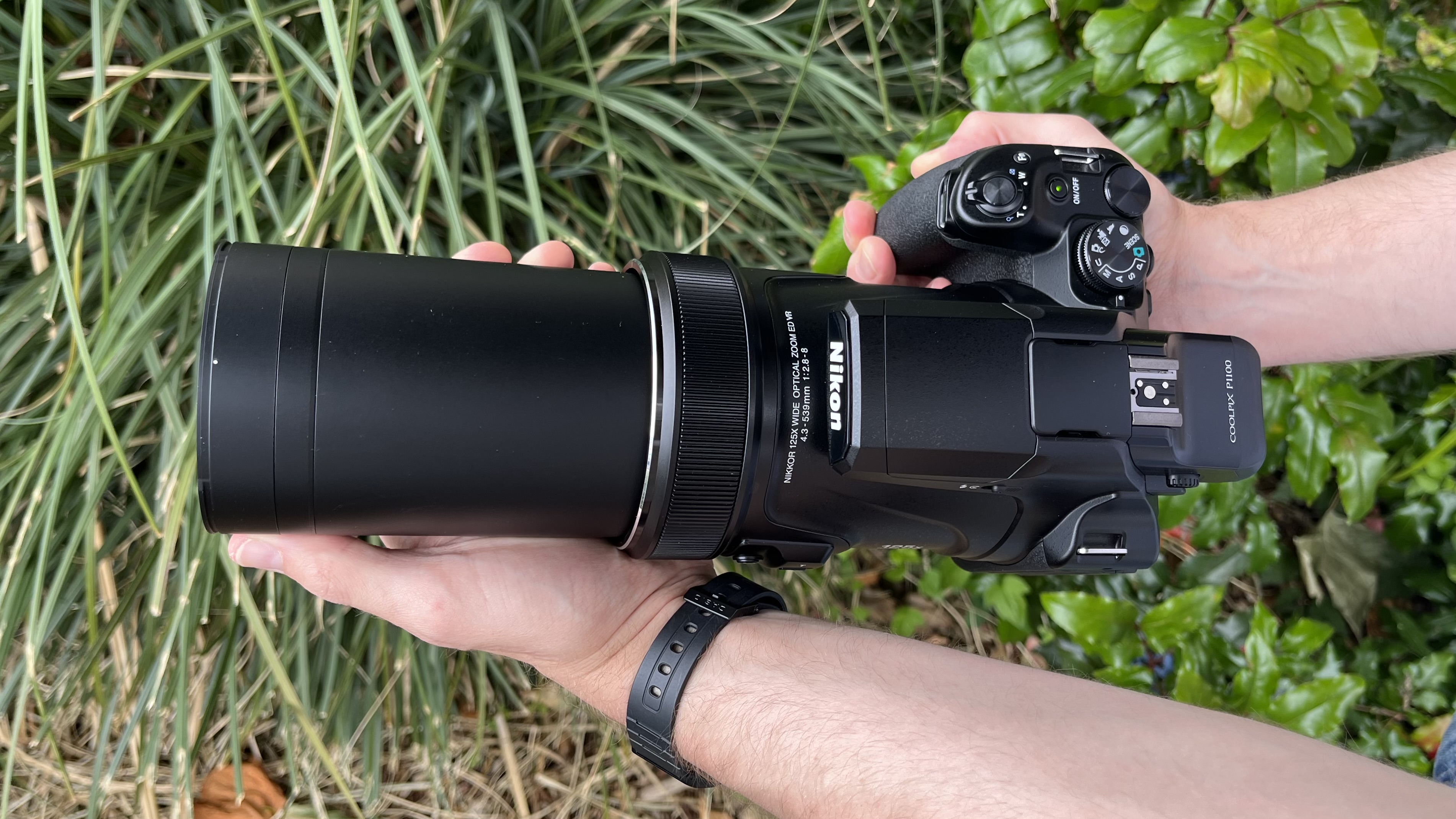Nikon Coolpix P1100 lifestyle image of hand holding the camera against green grasses