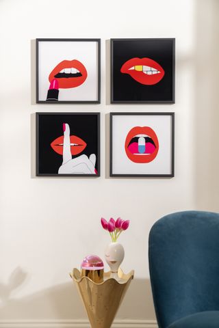 A living space with a cone shaped side table and four lip motif artworks hangings on the wall