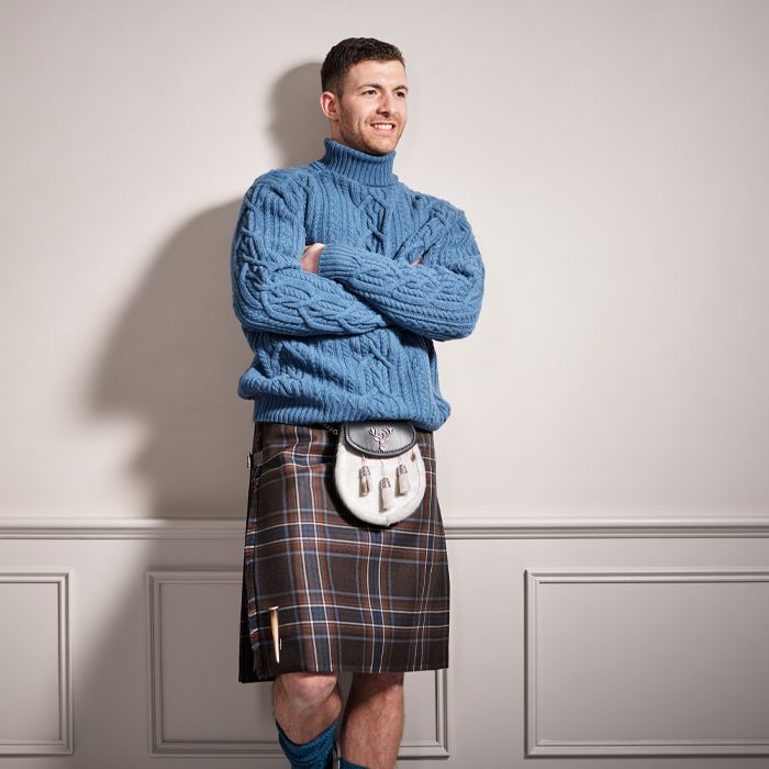 Man in blue cable knit jumper and kilt. He&#039;s leaning back against a wall