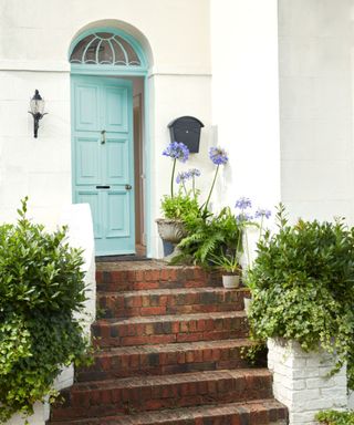 A light blue front door on a white house with brick front steps