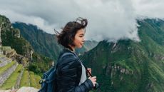 A woman stands high on a mountain with clouds in the distance