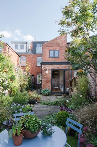 a rear house extension made from brick and glazed doors by mulroy architects, leading onto a wildlife garden with a small blue dining set at the end