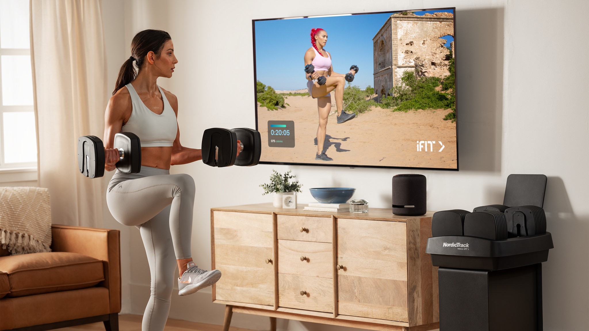 A person working out with the NordicTrack iSelect adjustable dumbbells while watching a virtual trainer take them through excercises