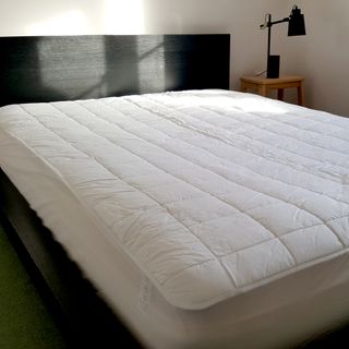 The Dreamland Snowed In Dual Control Heated Mattress Protector being tested on a double bed with a black headboard