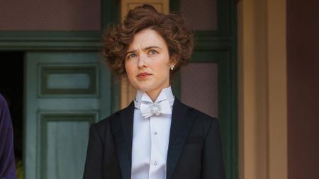 Sybilla wears a suit, standing in a doorway