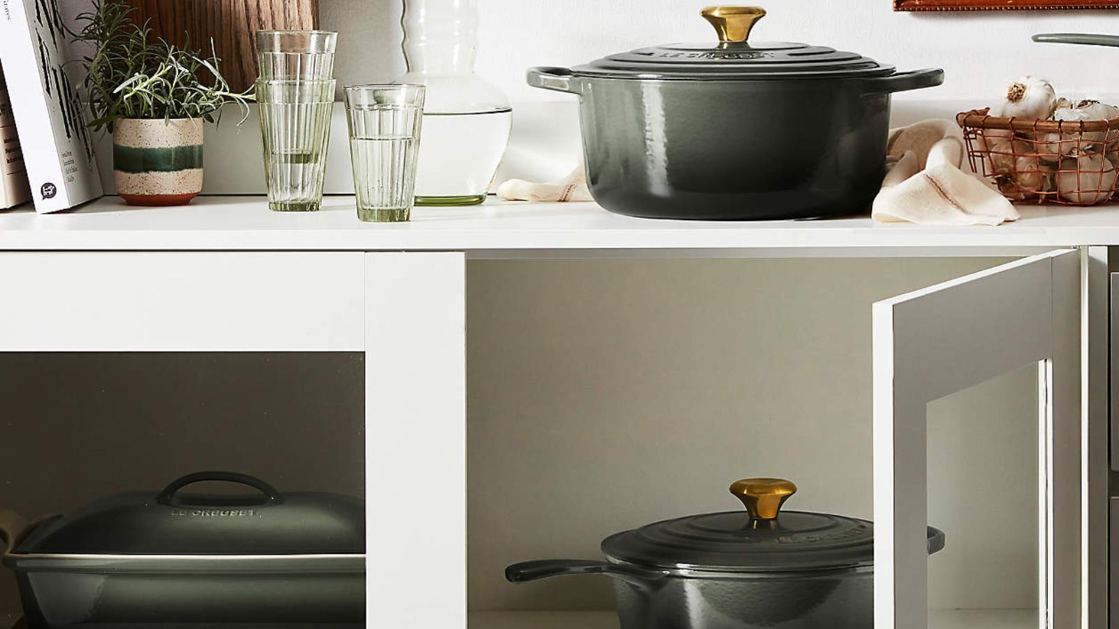 White kitchen dresser containing forest green Le Creuset dutch ovens