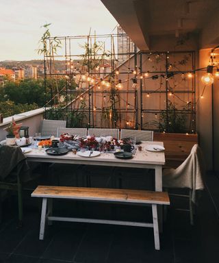 an outdoor table on a balcony set for entertaining with festive lights