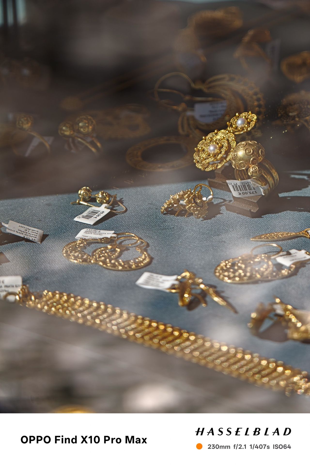 Gold jewelry and pearl earrings displayed behind a reflective shop window.