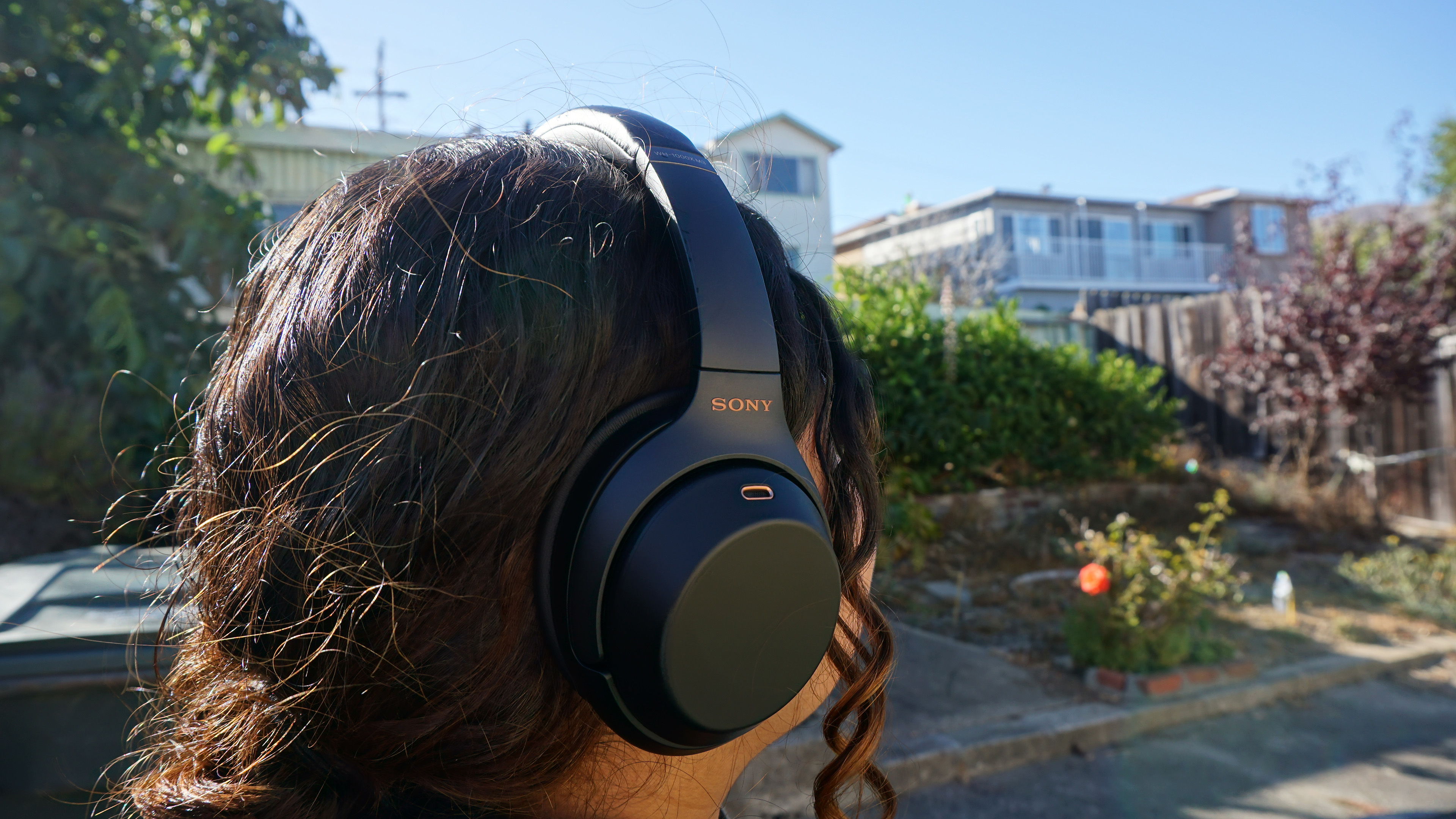 Seseorang yang memakai headphone Sony WH-1000XM3 di luar pada hari yang cerah