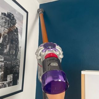 Using the Dyson combination tool in the corners of a white and blue painted bedroom