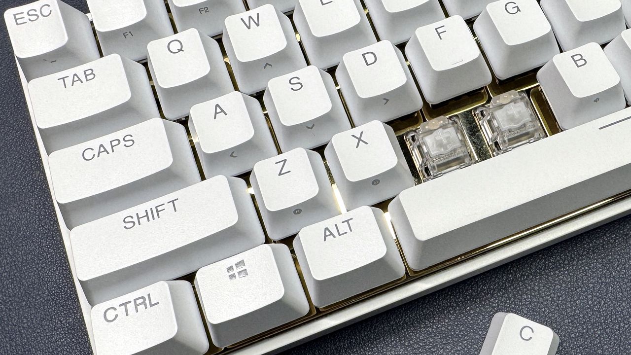 close up of white SteelSeries Apex Pro Mini with keycaps taken off to show brass plate