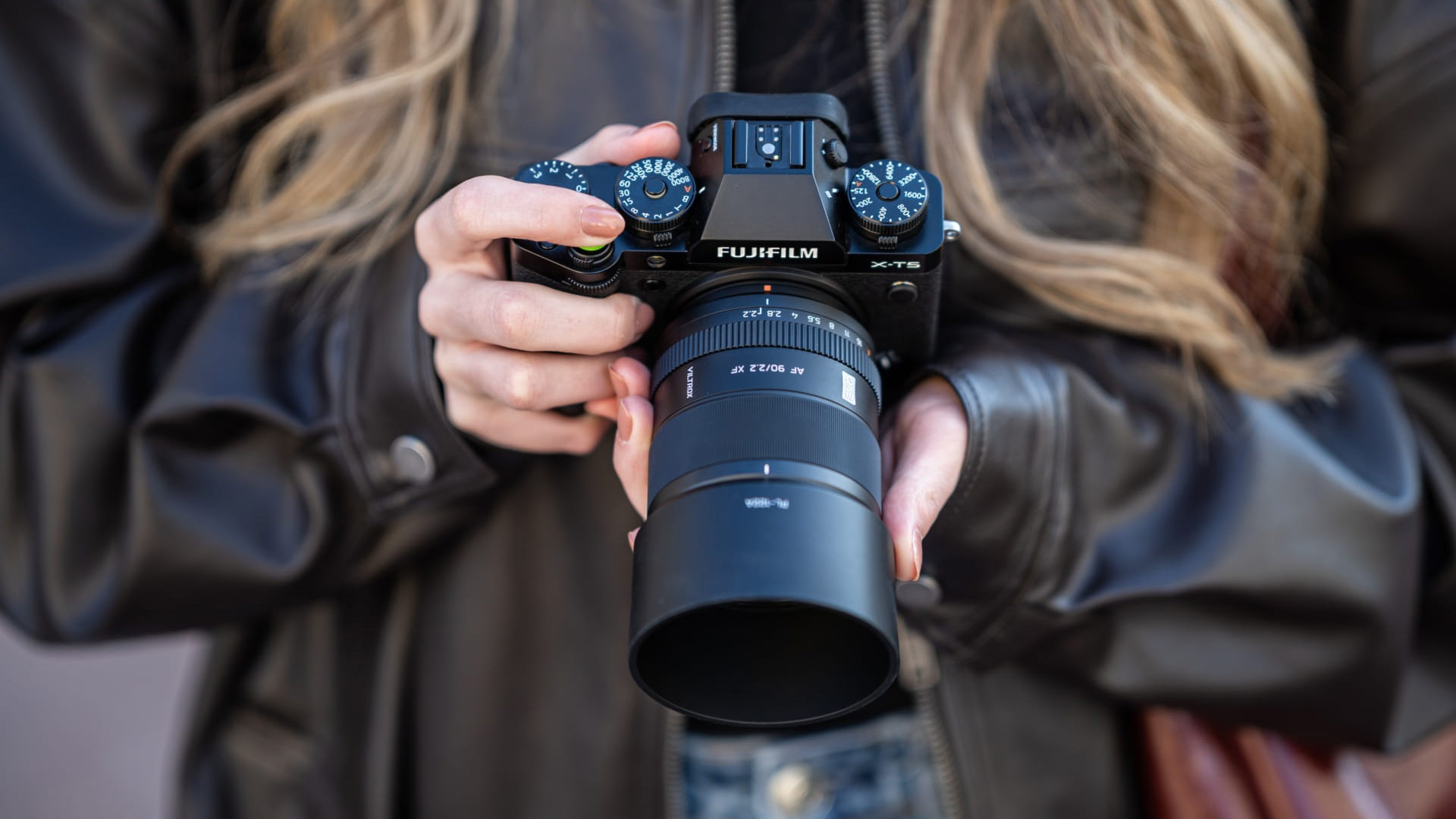 The Viltrox AF 75mm F1.8 EVO lens attached to a Fujifilm camera, held downwards by a photographer