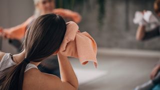 A woman wiping sweat off her face in a hot yoga class