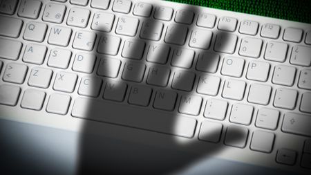 A menacing hand shadow on a computer keyboard in front of printed computer data.