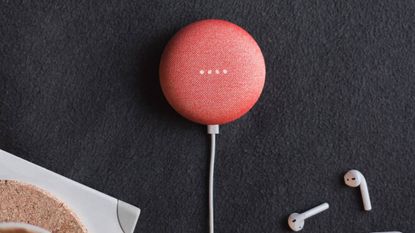 A red Google Nest Mini sitting on a table next to AirPods