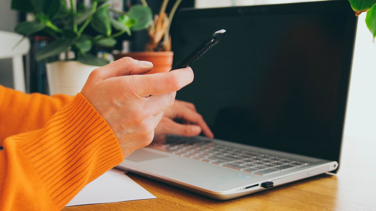 A person holds their smartphone while working on laptop.