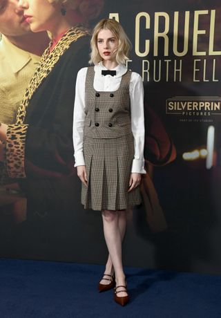 Lucy Boynton wears a plaid pleated skirt with matching vest.