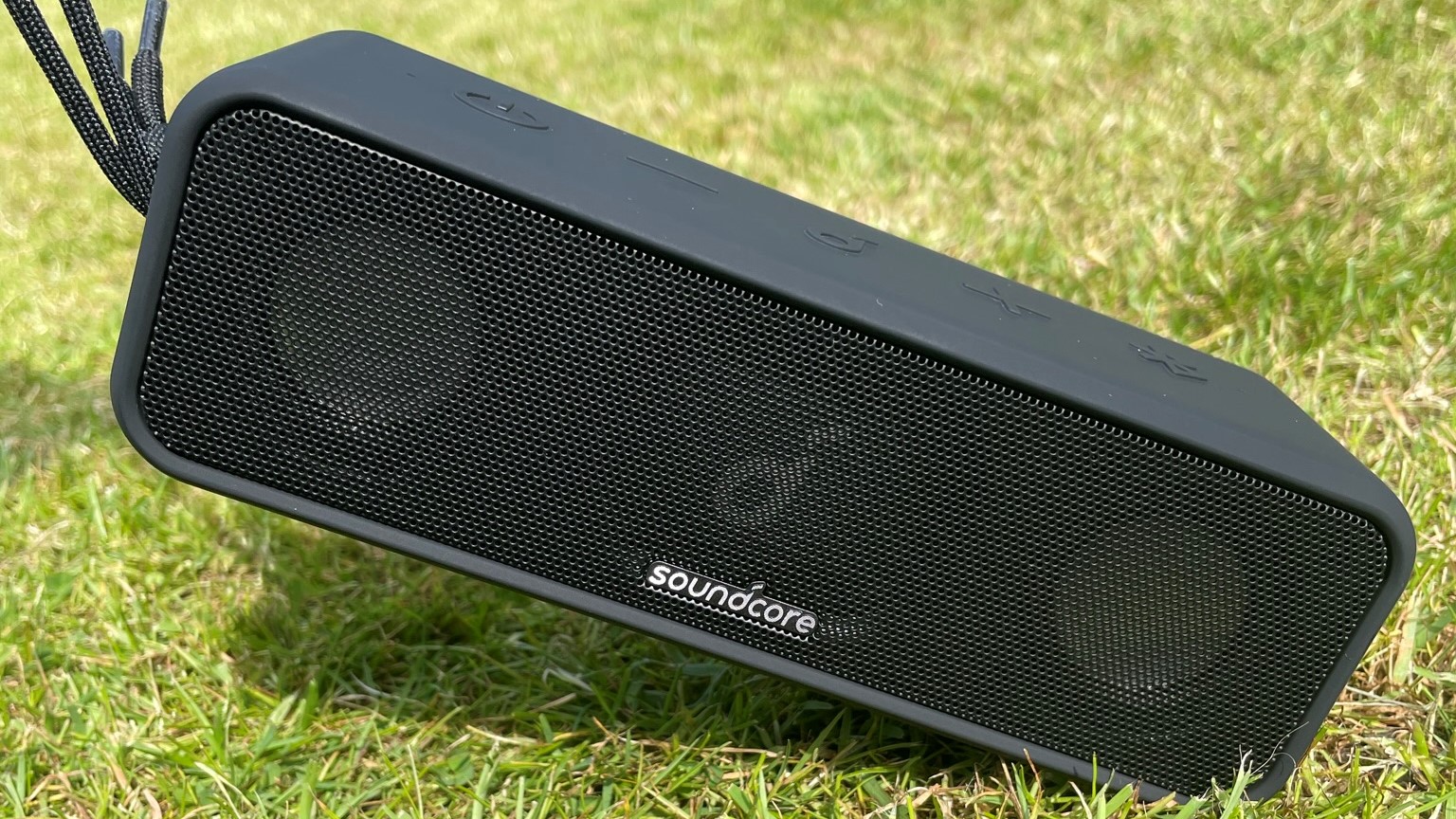 Portable speaker outside on grass being pulled up by strap on left side