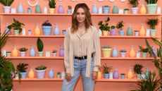 Ashley Tisdale standing in front of orange wall with pastel colored products including liquid soap dispensers and little and large plant pots