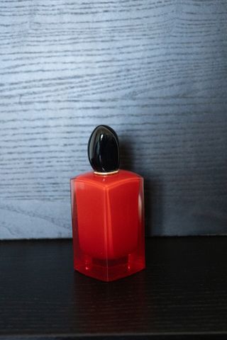 A red perfume standing in front and on top of a black ground