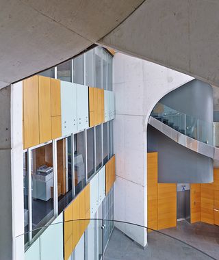 The interior view of the Cube1 showing 2 levels with glass, white and oak design; white walls and grey floors. The staircase has clear glass banister and silver metal base.