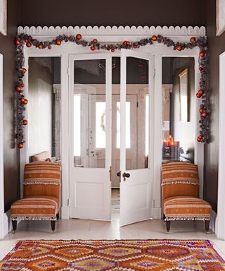 Inside view of large white front door with glass panels, decorated with green and red christmas garland, two orange occasional chairs and patterned rug