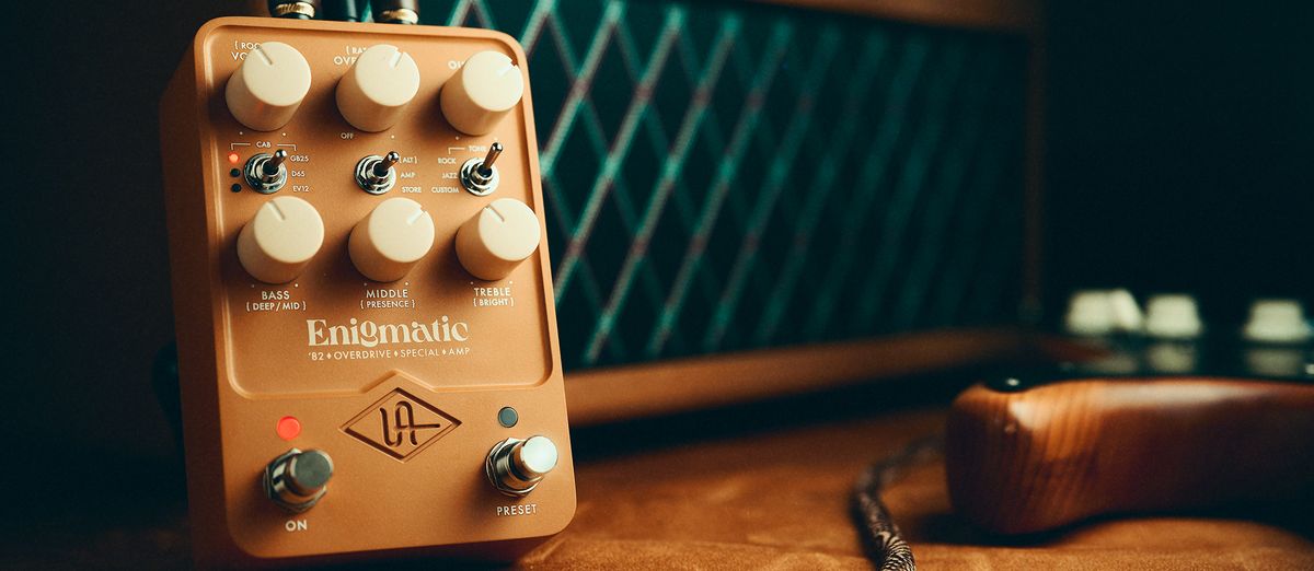 A photo of the Universal Audio Enigmatic ’82 Overdrive Special Amp pedal in shadow alongside a vintage Dumble amplifier and an electric guitar