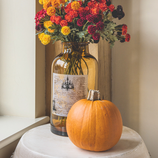 Pumpkin and vase on a white circular side table. Red, yellow and orange flowers are in the vase.