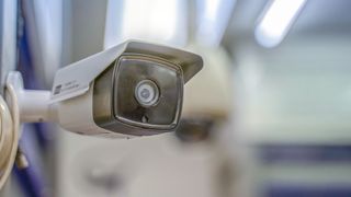 A close-up shot of a CCTV camera on a wall, in a brighly lit building