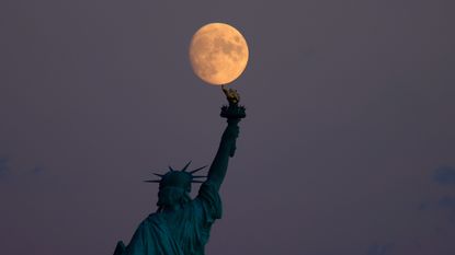 A 95 percent waxing crescent moon rises behind the Statue of Liberty in New York City on September 18, 2021 as seen from Jersey City, New Jersey.