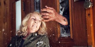 Laurie Strode (Jamie Lee Curtis) flinches as Michael Myers reaches through broken glass on a door in
