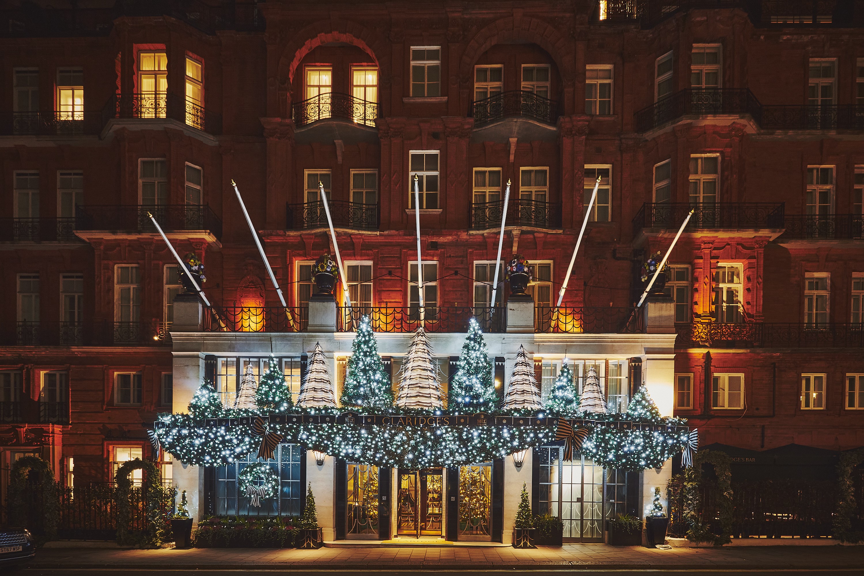 The historical brick exterior of a luxury hotel, captured adorned in Christmas decorations shaped like illuminated trees.