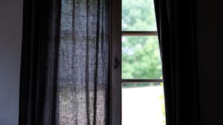 Black curtains partially covering window looking out into garden