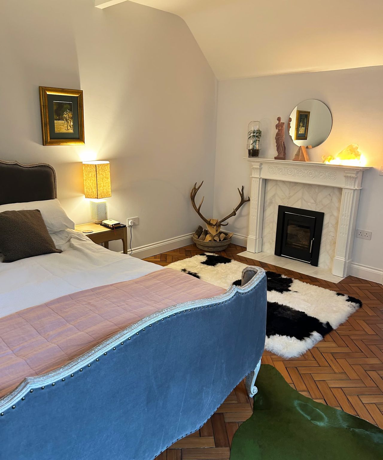 A bed next to a white marble fireplace with deer antlers in the corner