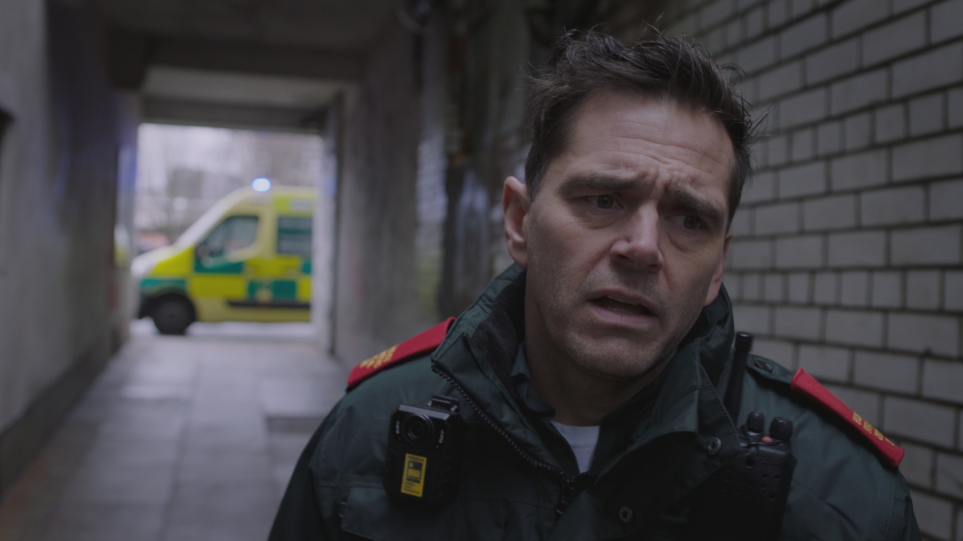 Paramedic Iain Dean stranding in an alleyway looking shocked with an ambulance in the background.
