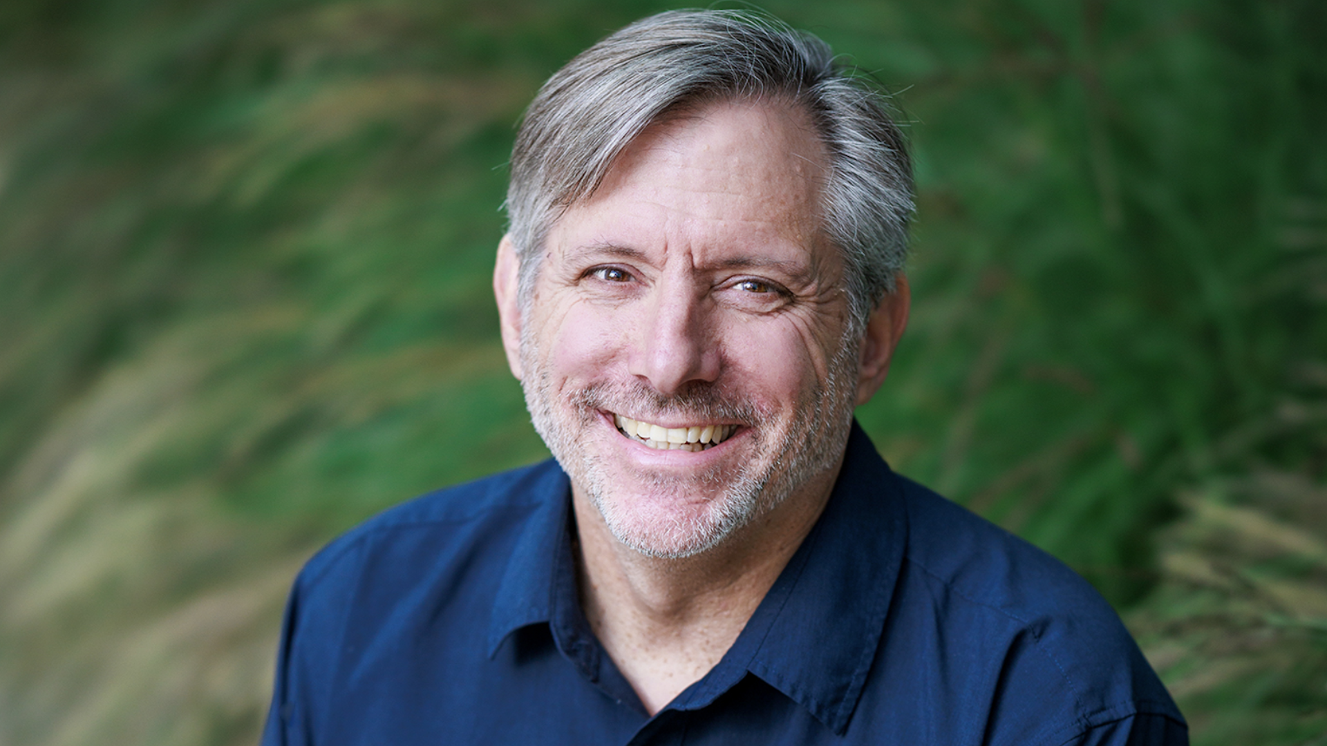 A shot of Brian Fleming, co-founder of Sucker Punch productions, smiling against a green natural background