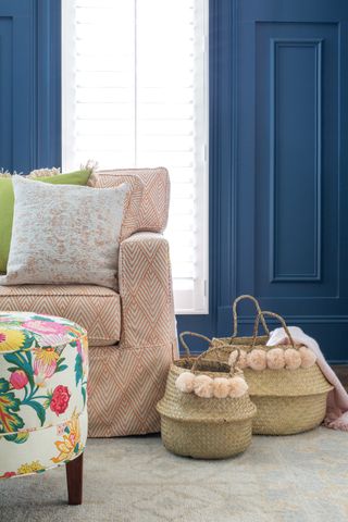 blue room with orange print couch, colorful footstool and two baskets with pompom trim