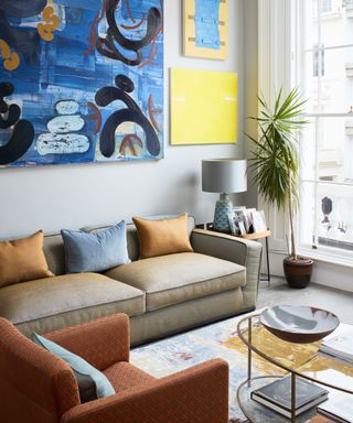 A white living room with orange and blue two-toned sofa, artwork and orange armchairs