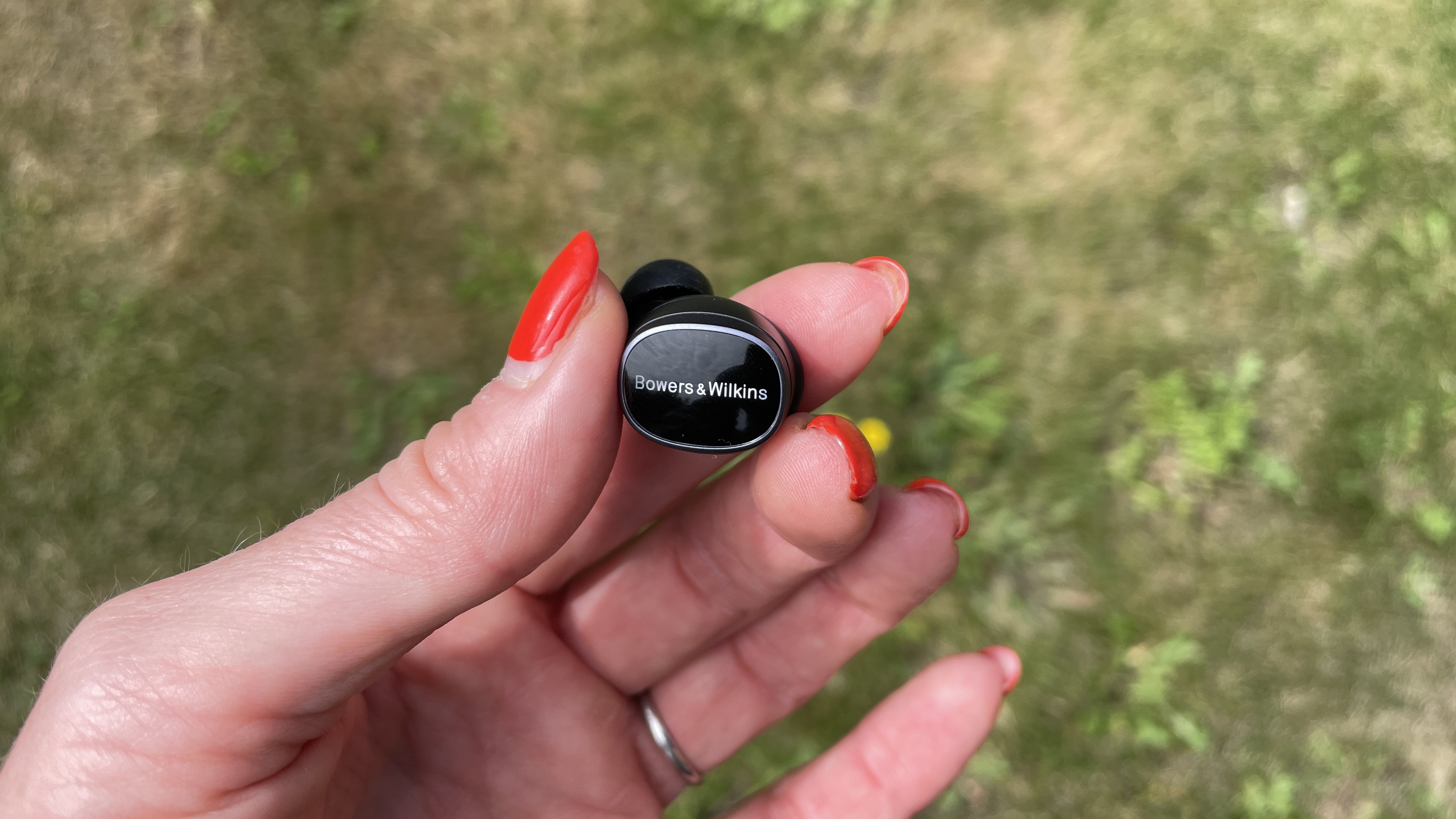 Bowers & Wilkins Pi8 earbuds, held in a hand on grassy background