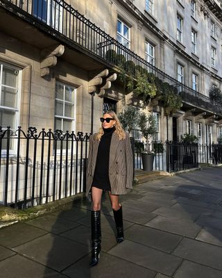 Woman wearing black minidress and oversize blazer with tall black boots.