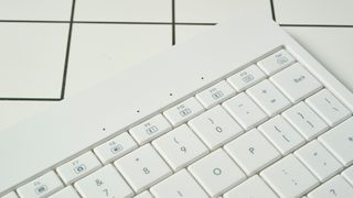 a closeup shot of the lights on a white, lightweight tablet keyboard made by mokibo rests upon a white tiled table with a blue background